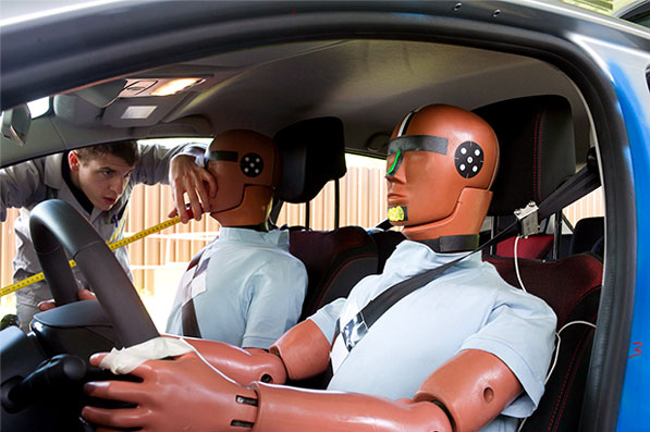 A man working inside a car with two crash test dummies.
